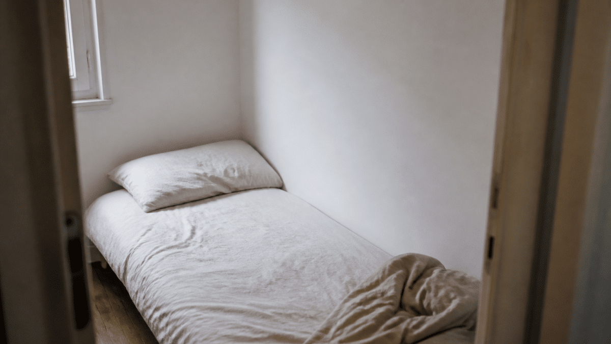 Petit lit simple contre mur blanc dans chambre etroite
